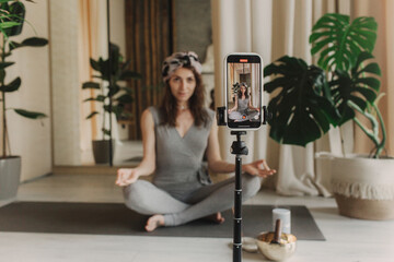 Live streaming on a smartphone - online yoga lesson. Beautiful woman training at home and watching...