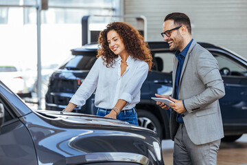 Woman in the showroom enjoying luxury car. Happy salesman selling the car to his female customer in...