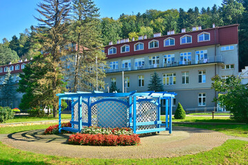 A wooden blue gazebo, located in a park in Rymanow Zdroj, Poland. Building of sanatorium in the background. - obrazy, fototapety, plakaty