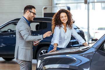 Woman in the showroom enjoying luxury car. Happy salesman selling the car to his female customer in a showroom. Auto business, car sale, consumerism and people concept