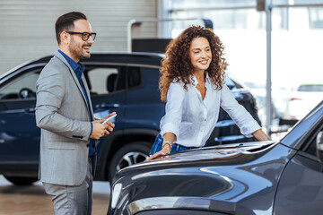 Woman in the showroom enjoying luxury car. Happy salesman selling the car to his female customer in...