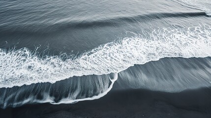 A serene sea of gentle waves on gray sand in a peaceful and contemplative atmosphere. Gray and dark beach sand in neutral tone in peaceful seaside scene.