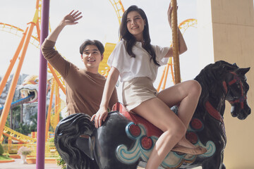 Young joyful couple man and woman riding on horse at Carousel amusement park. Concept happy and lovely life of teenager.