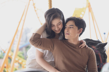 Obraz premium Young joyful couple man and woman riding on horse at Carousel amusement park. Concept happy and lovely life of teenager.