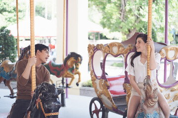 couple asian man and woman dating and riding on horse at Carousel amusement park. Concept happy and...