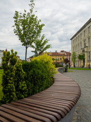 Curved wooden bench on city sidewalk next to vibrant green grass