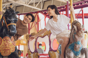 Obraz na płótnie Canvas couple asian man and woman dating and riding on horse at Carousel amusement park. Concept happy and lovely life of teenager.
