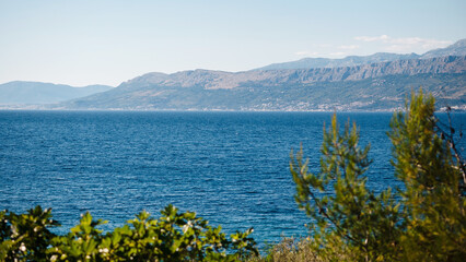 Fototapeta na wymiar Green tree tops with panoramic view on coast of Brac island. Fascinating landscape of beautiful clear Adriatic sea and high rocky mountains. Atmosphere of calmness.