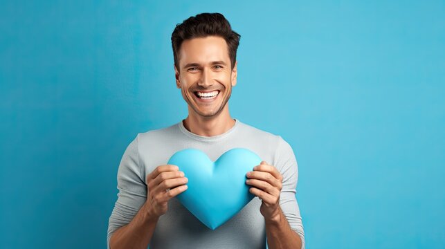 Smiling man holding small plastic heart isolated on blue background. AI Generated.