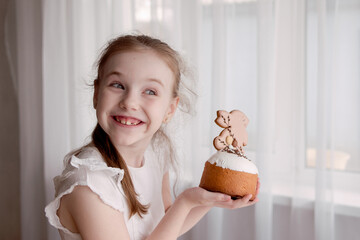 cute cheerful and mischievous girl with bunny ears smiles near Easter traditional Easter cakes with icing