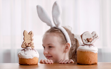 cute cheerful and mischievous girl with bunny ears smiles near Easter traditional Easter cakes with...