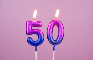 Pink and blue with white spots birthday candles burning on pink background. Number 50.	