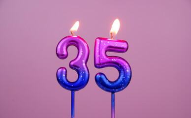 Colorful birthday candles burning on pink background. Number 35.