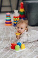 Fototapeta na wymiar Cute close-up of a baby lying on the floor and holding toys blocks, adorable baby 5 month old baby