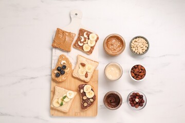 Toasts with different nut butters and products on white marble table, flat lay
