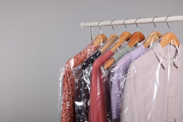 Dry-cleaning service. Many different clothes in plastic bags hanging on rack against grey background, space for text