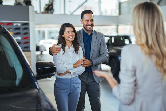 Car saleswoman assisting customers to make the best choice for buying a new car in the showroom. Young couple choosing new car for buying in dealership shop