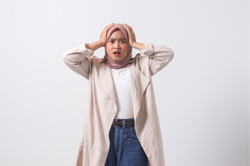 Portrait of frightened Asian hijab woman in casual suit holding head, showing surprised and scared...