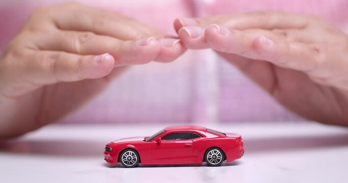 Close-up shot of hands hovering over a small toy red sportscar, manifesting a desire to own a new vehicle.
