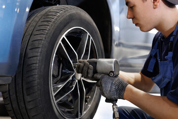 Car mechanic worker doing tire or wheel replacement with pneumatic wrench in garage of repair...