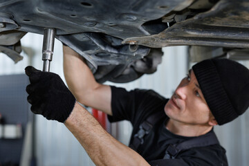 A mechanic inspecting or fixing the steering rack underneath the car at an auto repair shop. - obrazy, fototapety, plakaty