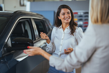 Businesswoman looking for a new car, standing next to a new SUV indoors at a car dealer. Beautiful...