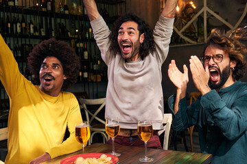Multiethnic group of three male friends watching soccer match at a bar. Celebrating happily a score...