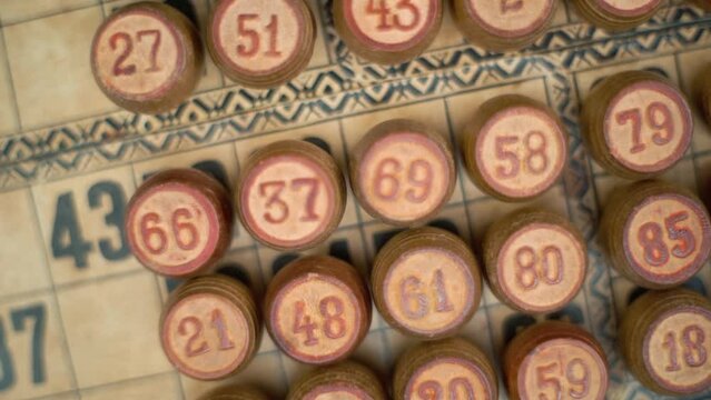 Cinematic close-up smooth zoom in rotating shot from above of Bingo wooden barrels in a row, woody figures, old numbers background, vintage board game, slow motion 120 fps commercial gimbal video