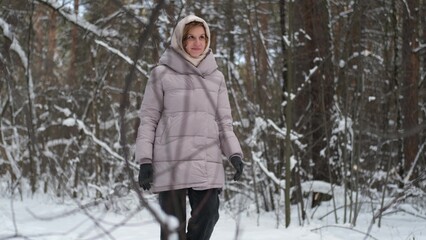 A young woman stands against a background of fir trees under a snowy forest in winter. A girl in a...