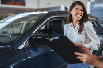 Car dealership manager helps a client choose a car. Female sales manager selling electric car to a...