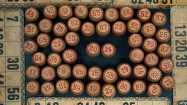 Cinematic close-up smooth shot from above of a pile of Bingo wooden barrels in a square, woody figures, old numbers background, vintage board game, slow motion 120 FPS commercial video pan left