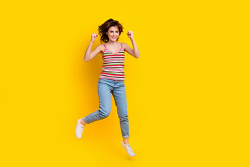 Fototapeta na wymiar Full body photo of ecstatic satisfied girl wear striped tank fly clenching fists win lottery isolated on vibrant yellow color background