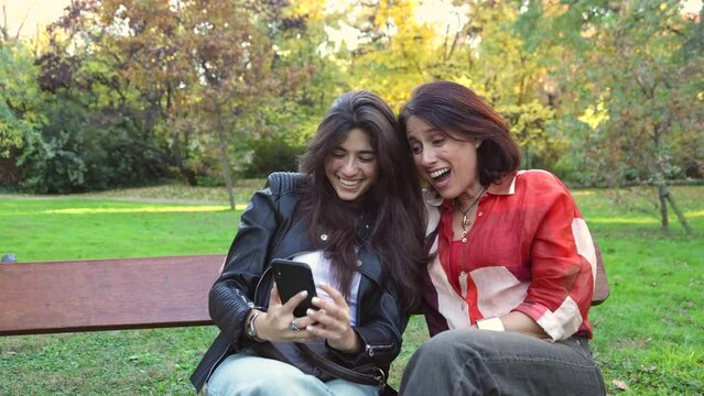 Happy young woman and adult woman taking a photo with a mobile phone sitting on a bench
