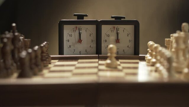 Chess game opening, pawn E2 to E4, female hand picks up chess piece and triggers chess clock