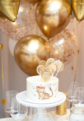 Decorated party table. Birthday cake with handpainted image of a little cat holding golden ballons