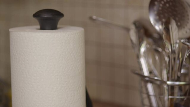 Close up of a hand ripping off a piece of paper towel next to a set of utensils in a kitchen.