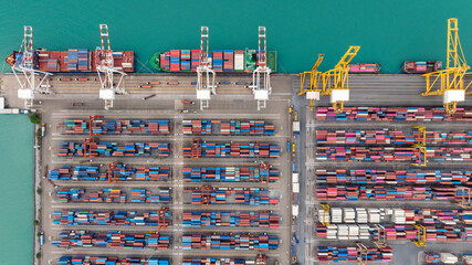 commercial port loading and unloading cargo from container ship import and export by crane for distributing goods by trailers transported to customers and dealers, aerial top view
