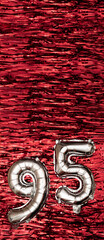 Silver foil balloon number 95 on a background of red tinsel decoration. Birthday greeting card,...