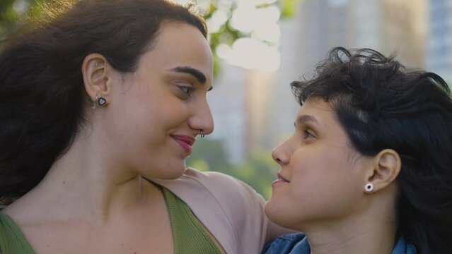 Portrait lesbian couple in love at city park looking each other with affection. Beautiful young gay love, feeling happiness tenderness. Calm family pair spending romantic weekend close up.
