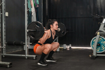 Girl in good physical condition doing squats with a barbell in the gym.