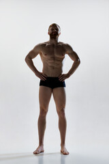 Fototapeta premium Full length portrait of young attractive man with perfect body curves posing in underwear against white background. Concept of natural beauty, aesthetic of body, male health, masculinity.