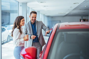 Shot of a young couple looking at cars at a car dealership.  It is the one car I want! Beautiful young couple standing at the dealership choosing the car to buy