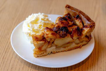 Selective focus of a piece of apple pie on white plate served with whipping cream on the side, Homemade apple pie on wooden table, Freshly baked.