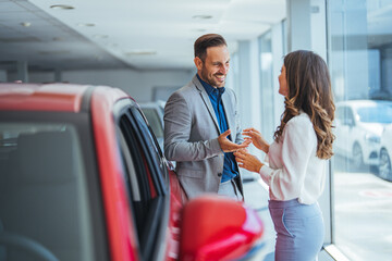 Shot of a young couple looking at cars at a car dealership.  It is the one car I want! Beautiful young couple standing at the dealership choosing the car to buy - obrazy, fototapety, plakaty