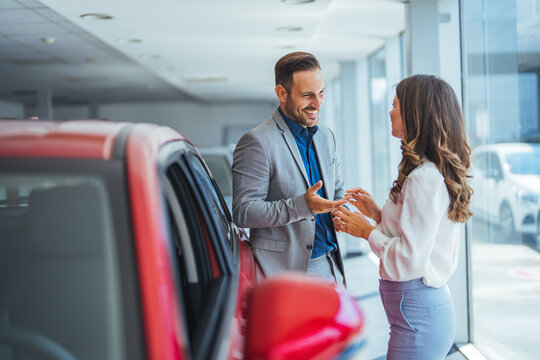 Portrait of a beautiful young couple choosing a new car at a car dealership. Buying a long-awaited car. Couple buying the car. Pair in a car salon. Husband with vife choose the automobile