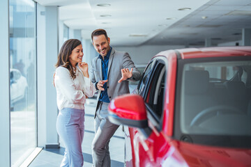 This car is exactly what we want. Beautiful young couple standing at the car dealership and making...