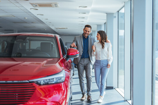 Portrait of a beautiful young couple choosing a new car at a car dealership. Buying a long-awaited car. Couple buying the car. Pair in a car salon. Husband with vife choose the automobile
