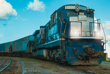 Blue locomotive with wagons making the turn on the railroad track. Blue sky with white clouds in the background.