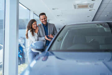 Beautiful young couple at car showroom choosing a new car to buy. Happy beautiful couple is...