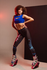 Sporty slim woman in leggings and top wearing kangoo jumper and posing in studio on background - 718041271